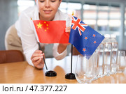 Young woman putting China and New Zealand flags on table in office. Стоковое фото, фотограф Яков Филимонов / Фотобанк Лори