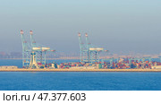 Manama, Bahrain - Jan 08 2024, Panoramic view of Bahrain commercial international  port with blue cranes, pier, buildings and containers, with sea on foreground, at daytime, Manama, Bahrain. Редакционное фото, фотограф Сергей Богомяко / Фотобанк Лори