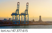 Manama, Bahrain - Jan 08 2024, Panoramic view of Bahrain commercial port with blue cranes, buildings and containers, with sea on foreground, by the morning, dawn, sunrise, Manama, Bahrain. Редакционное фото, фотограф Сергей Богомяко / Фотобанк Лори