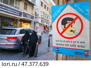 Manama, Bahrain - Jan 08 2024, A view of the street with pedestrians, half of the frame is occupied by a warning sign prohibiting spitting, Manama, Bahrain. Редакционное фото, фотограф Сергей Богомяко / Фотобанк Лори