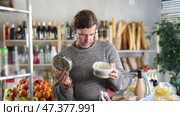 Casually dressed male shopper examining two plastic containers of pickled herring in grocery store, carrying shopping basket filled of various foods on arm. Стоковое видео, видеограф Яков Филимонов / Фотобанк Лори
