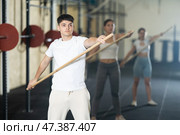Young guy, together with other athletes, does a warm-up using a long stick in gym. Стоковое фото, фотограф Яков Филимонов / Фотобанк Лори