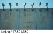 Surveillance cameras on a concrete wall, symbolizing border control and security. Ряды камер наблюдения, установленных на высокой бетонной стене, символизирующей пограничный контроль и безопасность. Стоковое AI-изображение, AI-художник Katsiaryna Repich / Фотобанк Лори