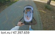 A parent is pushing a baby stroller along a paved path in a park. The child is dressed in a colorful overalls with different patterns lying on its back. A family walk in the park. Стоковое видео, видеограф Воловодов Владимир / Фотобанк Лори