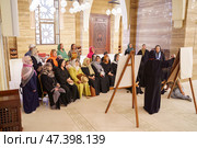 Manama, Bahrain - Jan 15 2024, An Arab woman dressed in a black burqa and niqab enthusiastically tells group of tourists about history of Islam inside of the Grand Mosque Al Fateh, Manama, Bahrain. Редакционное фото, фотограф Сергей Богомяко / Фотобанк Лори
