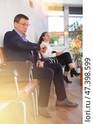 Serious-minded male candidate siting on chair and waiting for job interview in hallway. Стоковое фото, фотограф Яков Филимонов / Фотобанк Лори