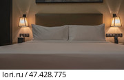 The bedroom is ready for sleep. The double bed is neatly made with white sheets. Pillows at the headboard. The wall sconces are lit. Soft evening lighting. A box of napkins on the bedside table. Стоковое фото, фотограф Вера Ивановна Кубарева / Фотобанк Лори