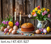 Православная Пасха. Пасхальный кулич, крашеные яйца, цветы, церковные свечи и пасхальный декор на деревянном столе в старом деревенском доме. Стоковое AI-изображение, AI-художник Руслан Лесков / Фотобанк Лори
