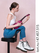 Woman holding ukulele and tuning strings of her musical instrument with concentration. Profile view. Стоковое фото, фотограф А. А. Пирагис / Фотобанк Лори