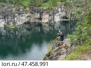 Hiker perching near canyon edge, arms raised, savoring panoramic landscape of flooding marble quarries in ruskeala mountain wilderness. Стоковое фото, фотограф Mikhail Davidovich / Фотобанк Лори