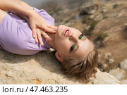 Splendid female fashion model lies on back on rock, places both palms on neck and looks at camera. Стоковое фото, фотограф А. А. Пирагис / Фотобанк Лори