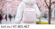 Spring outing: woman with a pink backpack amidst blooming cherry trees. Стоковое AI-изображение, AI-художник Данила Большаков / Фотобанк Лори