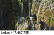 Natural water flowing down mossy rocks, creating a beautiful waterfall in a lush green forest, showcasing the tranquility and beauty of nature. Стоковое видео, видеограф ILIA GOROKHOV / Фотобанк Лори