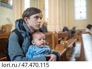 12-летний мальчик сидит со своим младшим братом на скамейке в католической церкви во время детской мессы. Редакционное фото, фотограф Яна Проничева / Фотобанк Лори