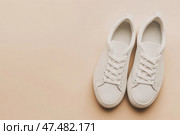 White leather lace-up running shoes with low tops, thick soles on a beige. The laces and rubber outsole. Sporty look. Men to wear during outdoor activities. Street hiking shoes. Trendy Male Boots Pair. Стоковое AI-изображение, AI-художник Марина Демидюк / Фотобанк Лори