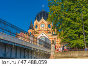 The new synagogue of Kaliningrad, majestically towering over the Pregolya embankment. The photo was taken from a low point near the bridge - in the foreground you can see the openwork metal fence and passers-by on the bridge. The synagogue building itself is decorated with stained glass windows, patterns and a striped facade of light and dark brick. The dome is crowned with the Star of David. A bright sunny day and a rich blue sky give the photo a lively and warm atmosphere. (2020 год). Редакционное фото, фотограф Анна Кривицкая / Фотобанк Лори