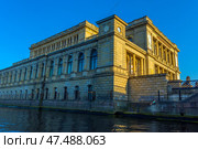The majestic building of the Kaliningrad Regional Museum of History and Art, located on the bank of the Pregolya River. The architecture of the building is done in the neo-Renaissance style with elements of classicism: high arched windows, colonnades, decorative cornices and a clock tower. The light of the evening sun softly illuminates the facade, creating a warm atmosphere and emphasizing the details of the stonework. In the foreground you can see the embankment, stairs and a fragment of a forged fence. The building is reflected in the calm river water. (2020 год). Редакционное фото, фотограф Анна Кривицкая / Фотобанк Лори