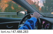 A close-up of a man's hand loosely holding steering wheel of a car. In background is a dashboard with speedometer and tachometer. Behind car windows a beautiful mountain landscape in sunset light. Стоковое видео, видеограф Воловодов Владимир / Фотобанк Лори