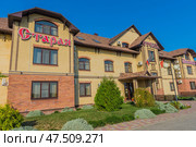 A cozy country hotel with the traditional name "Old Mill", located in the village of Kushchevskaya. The building is made of light and red brick, the roof is covered with brown tiles. The windows are arched, with decorative brick edging. The hotel grounds are well-kept - thujas, shrubs, lush greenery and ornamental plants are planted along the facade. Bright blue weather, a sunny day and a clear sky emphasize the pleasant atmosphere and attractiveness of the place. Signs are visible: "Old", "Hotel", "Mill". hotel (2020 год). Редакционное фото, фотограф Анна Кривицкая / Фотобанк Лори