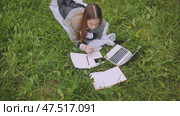 A young student with notebooks and a laptop lying on the grass. Стоковое видео, видеограф Mikhail Davidovich / Фотобанк Лори