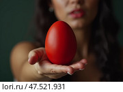 Женщина держит красное пасхальное яйцо на вытянутой руке. Стоковое AI-изображение, AI-художник Анна Рогалева / Фотобанк Лори
