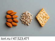 A minimalist snack display features roasted almonds, sunflower seeds, and sesame crackers meticulously arranged. The geometric precision of this setup highlights the art of food presentation. Стоковое AI-изображение, AI-художник Nart / Фотобанк Лори