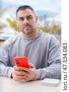 Man typing on red smartphone while sitting outdoors near palm trees and port. Стоковое фото, фотограф Raquel Corcoles Mendez / Фотобанк Лори
