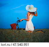 Beautiful young woman in white dress and hat with bicycle in wheat field. Стоковое фото, фотограф Nobilior / Фотобанк Лори