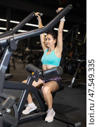 In gym, woman uses lat pulldowm machine to strengthen arm muscles. Стоковое фото, фотограф Яков Филимонов / Фотобанк Лори