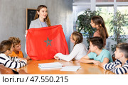 Group of curious preteen learners and young female teacher with flag of Morocco in classroom of academy. Стоковое фото, фотограф Яков Филимонов / Фотобанк Лори