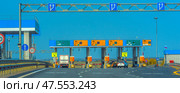 Toll booth on the M4 Don toll road in Russia. In the foreground, a truck passes through a barrier in a special lane with a green arrow, intended for transponders (automated payment system). Above each lane, there are electronic boards with payment methods (cash, card, transponder) and accessibility information. The infrastructure is clearly organized: road signs, fences, CCTV cameras, and safety signs. In the background, there is an open rural landscape with fields and trees on the horizon. (2020 год). Редакционное фото, фотограф Анна Кривицкая / Фотобанк Лори