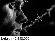 Close-up of person contemplating life with barbed wire in black and white. Человек задумчиво смотрит вдаль, подчеркивая сильные эмоции. На переднем плане видна колючая проволока, символизирующая конфликт или борьбу. Изображение запечатлело мощный момент размышления. Стоковое AI-изображение, AI-художник Katsiaryna Repich / Фотобанк Лори