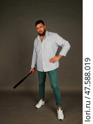 Bearded Man With a Confident Stance Holding a Bat in a Minimalist Indoor Studio Setting. Стоковое фото, фотограф Aleksandr Golubev / Фотобанк Лори