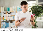 Attentive interested young guy client choosing between two boxes of paracetamol antipyretic pills in drug store. Стоковое фото, фотограф Яков Филимонов / Фотобанк Лори
