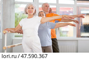 Dancing positive elderly women and men engaged in group class perform exercise near ballet barre, standing in 2nd position of ballet stance in dance studio. Стоковое фото, фотограф Яков Филимонов / Фотобанк Лори