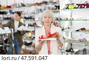 Mature woman client is demanding to inspect sandals in shoe showroom. Стоковое фото, фотограф Яков Филимонов / Фотобанк Лори