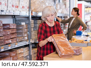 Elderly woman buys briquettes with red clay in specialized store. Стоковое фото, фотограф Яков Филимонов / Фотобанк Лори