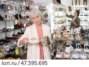 Positive mature female customer holds in hands and compares slippers. Стоковое фото, фотограф Яков Филимонов / Фотобанк Лори