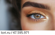 Beautiful close-up of a woman's eye with shimmering gold eyeshadow and defined brows. Стоковое AI-изображение, AI-художник Сергей Толмачёв / Фотобанк Лори