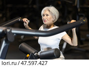 In gym, senior woman uses lat pulldowm machine to strengthen arm muscles. Стоковое фото, фотограф Яков Филимонов / Фотобанк Лори