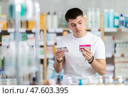 Attentive interested young guy client choosing between two boxes of paracetamol antipyretic pills in drug store. Стоковое фото, фотограф Яков Филимонов / Фотобанк Лори