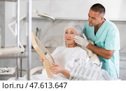 Male plastic surgeon giving professional advice after facial contouring to senior woman client looking at mirror. Стоковое фото, фотограф Яков Филимонов / Фотобанк Лори