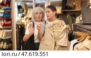 Pleased young and old ladies choosing beige vest in clothing shop with large assortment. Стоковое видео, видеограф Яков Филимонов / Фотобанк Лори