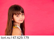A young girl with long hair smiles softly while looking back over her shoulder, set against a bright pink background. She embodies innocence and charm, making the moment delightful and engaging. Стоковое фото, фотограф Aleksandr Golubev / Фотобанк Лори