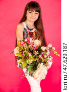 A young girl with flowing hair stands confidently while clutching a bouquet of colorful flowers. The vivid pink background enhances her cheerful expression, capturing a joyful moment. Стоковое фото, фотограф Aleksandr Golubev / Фотобанк Лори