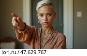 A Young Woman With a Short Blonde Hairstyle is Pointing Decisively While Gazing at the Camera. Стоковое AI-изображение, AI-художник Sergey Grishin / Фотобанк Лори