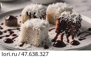 A plate of vegan lamingtons arranged on a light-colored surface, with chocolate sauce drizzling over the top and coconut flakes sprinkled around. The scene includes small bowls of coconut and chocolate chunks to emphasize the dessert’s plant-based ingredients. Стоковое AI-видео, аниматор Ирина Старикова / Фотобанк Лори