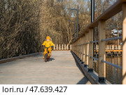 A cute boy in bright yellow clothes rides a bike. A happy child plays outside in early spring. Happy childhood. Стоковое фото, фотограф Photojuli / Фотобанк Лори