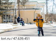 A little boy in bright yellow clothes rides a scooter. A happy child walks outside in early spring. Happy childhood. Стоковое фото, фотограф Photojuli / Фотобанк Лори