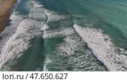 Aerial view capturing rhythmic turquoise waves rolling, breaking against golden sandy shoreline, showcasing powerful oceanic motion. Стоковое видео, видеограф ILIA GOROKHOV / Фотобанк Лори